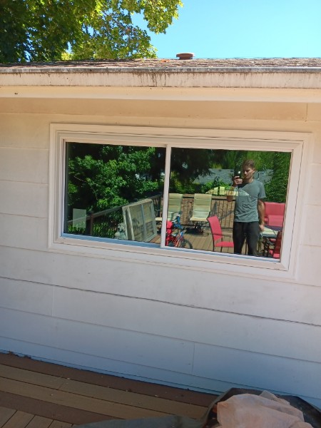 Wide white slider on a single-story ranch with deck furniture reflected in the glass